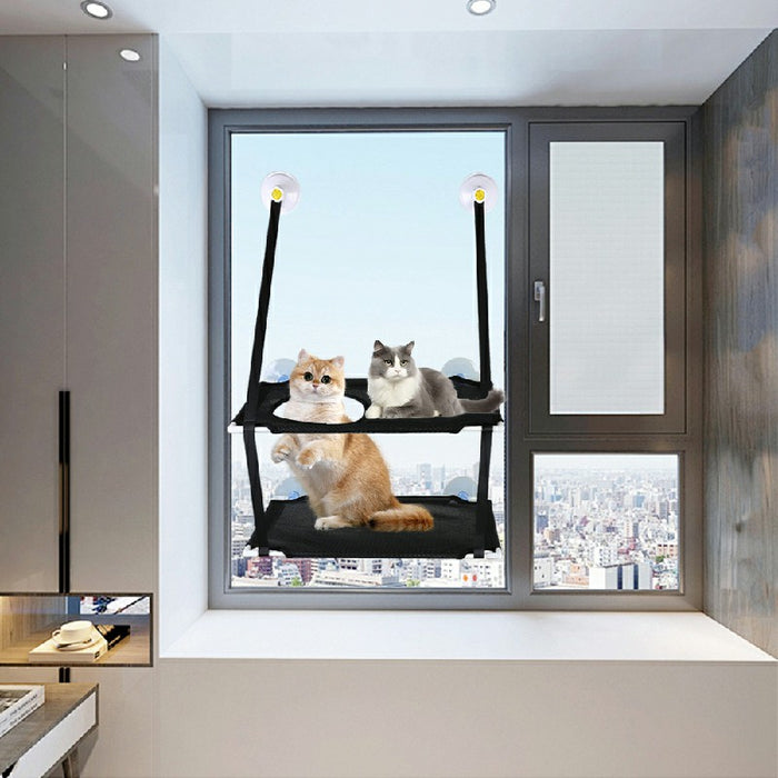 A black pet hammock for windows, featuring two cats resting on it with a cityscape view in the background.