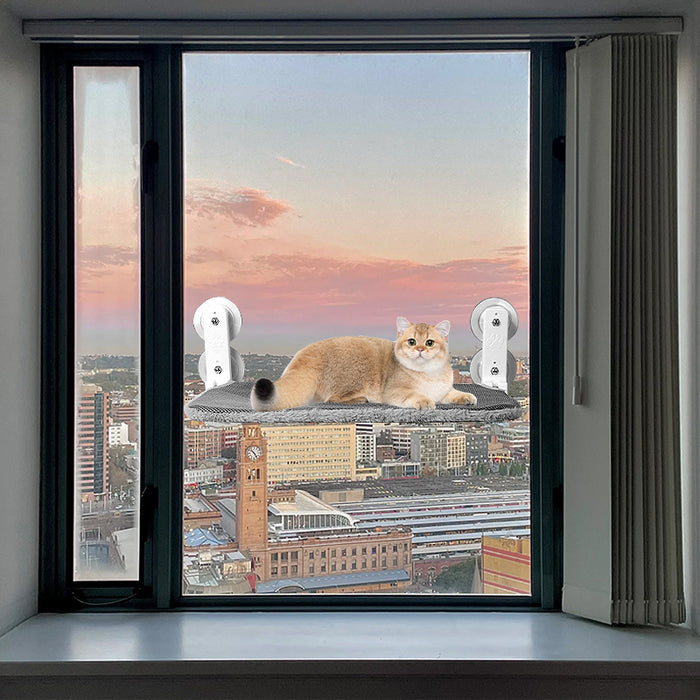 Gray cordless folding cat hammock on a window, featuring a cat lounging on it against a city skyline at sunset.