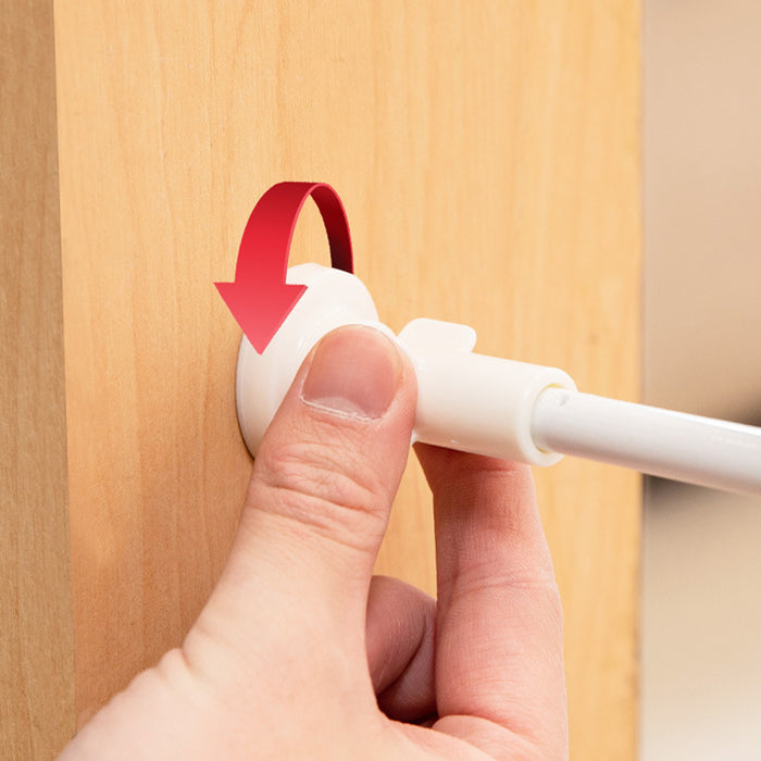 A hand is gripping a white retractable pet safety gate mechanism mounted on a wooden surface.