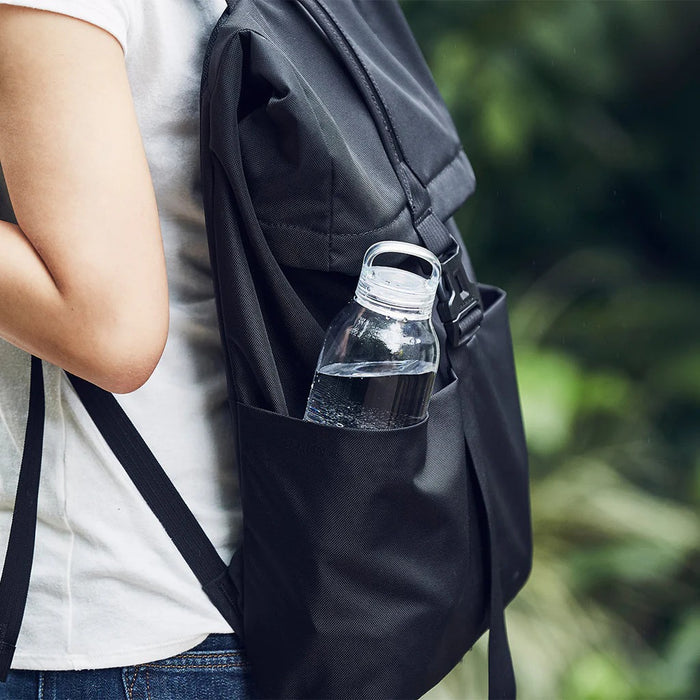 Person with a black backpack holding a clear water bottle outdoors